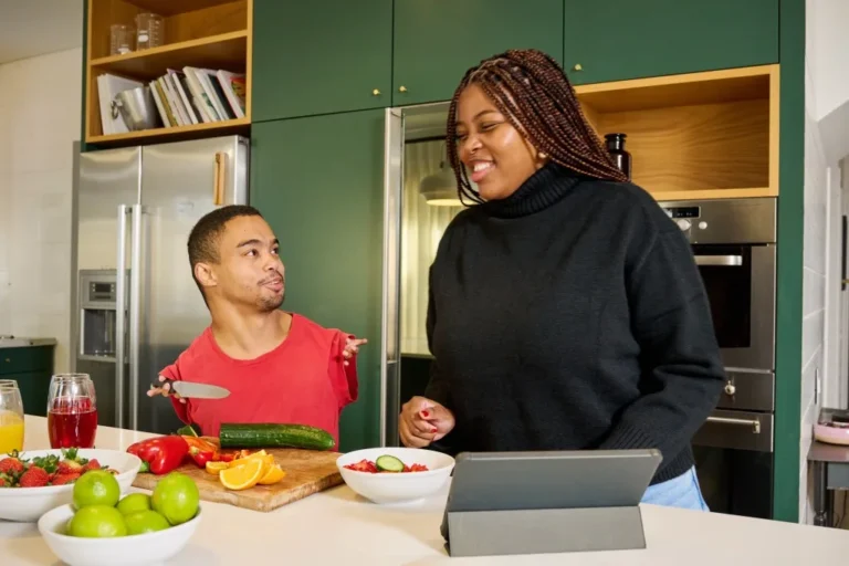 Disabled man in kitchen chopping vegetables with support worker