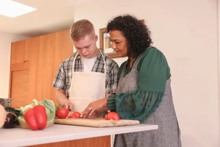 Support worker chopping vegetables in kitchen with disabled boy