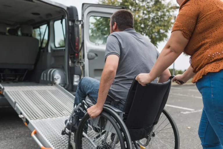 Disabled man in wheelchair being pushed up ramp into disability van by support worker