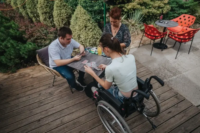 Two disabled friends playing card game with support worker